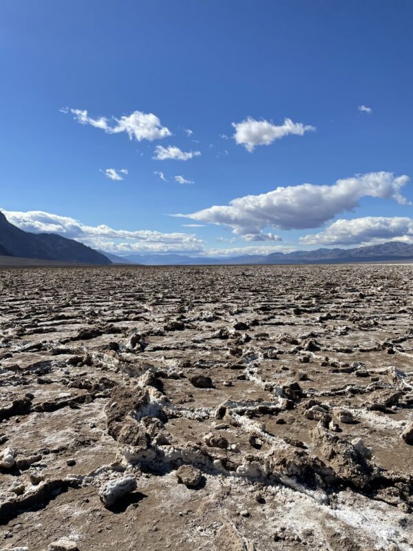 The cracked salt flats of Badwater Basin under a blue sky, with mountains beyond