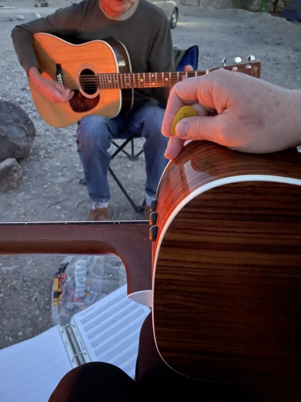 A guitar in the foreground and a campground neighbour playing his own guitar across from it