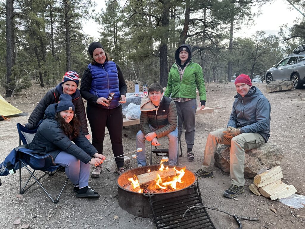 GRCA - Campfire with family Six people in winter coats and hats gathered around a campfire at the Grand Canyon campsite