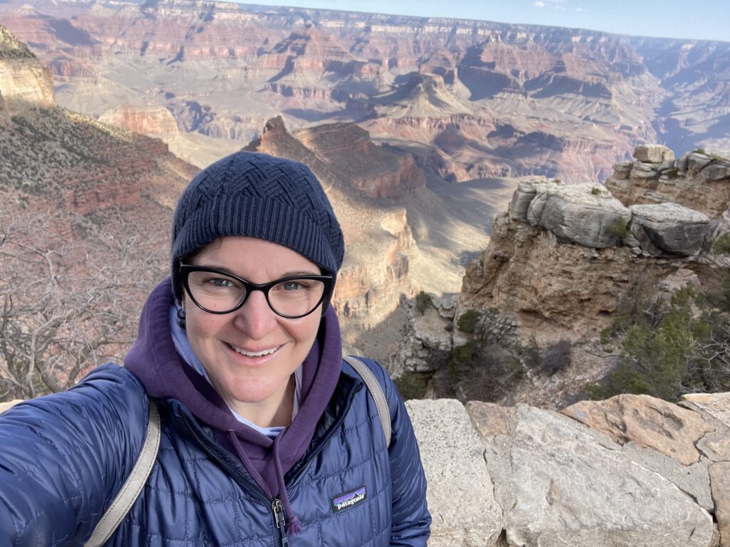 GRCA - Missy and canyon behind her Missy in a knit hat and coat smiling at the camera with the Grand Canyon behind her