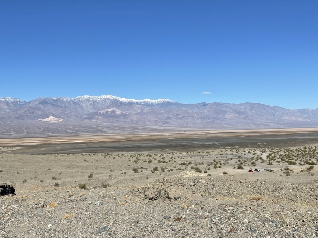A wide view across the Death Valley floor to a snow-topped range under a hard blue sky